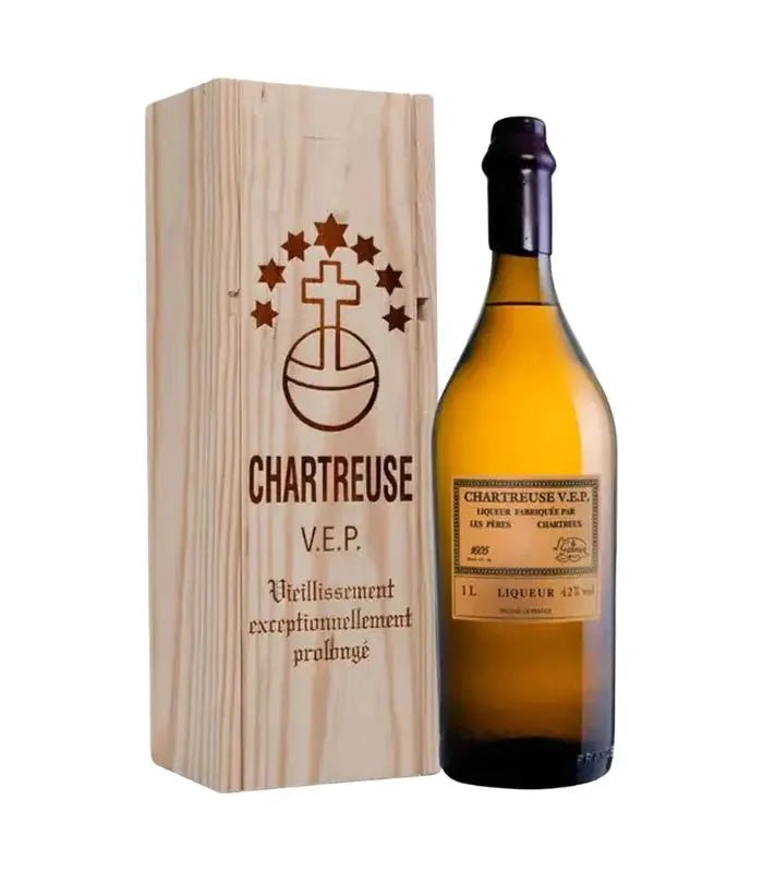 A bottle of Chartreuse Yellow V.E.P. Liqueur by Chartreuse stands next to its wooden box, elegantly engraved with the brand logo and French descriptions—making it an exceptional selection for luxury gifting.