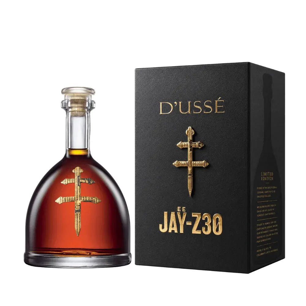 A bottle of D’USSE VSOP Jay-Z30 Limited Edition Cognac (PRE-ORDER) by D’USSÉ is displayed with a gold cross emblem next to a black box featuring gold lettering, reflecting the luxury of this limited-edition French cognac.