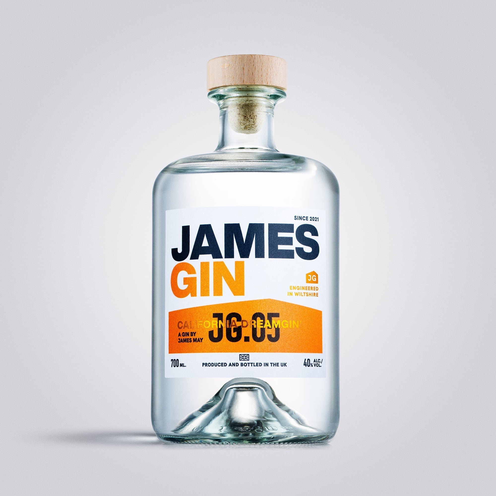 A clear glass bottle of James Gin California Dreamgin' by James Gin, featuring a wooden cap and white label with bold blue and orange text, is shown with a souvenir gift key chain against a plain light gray background.
