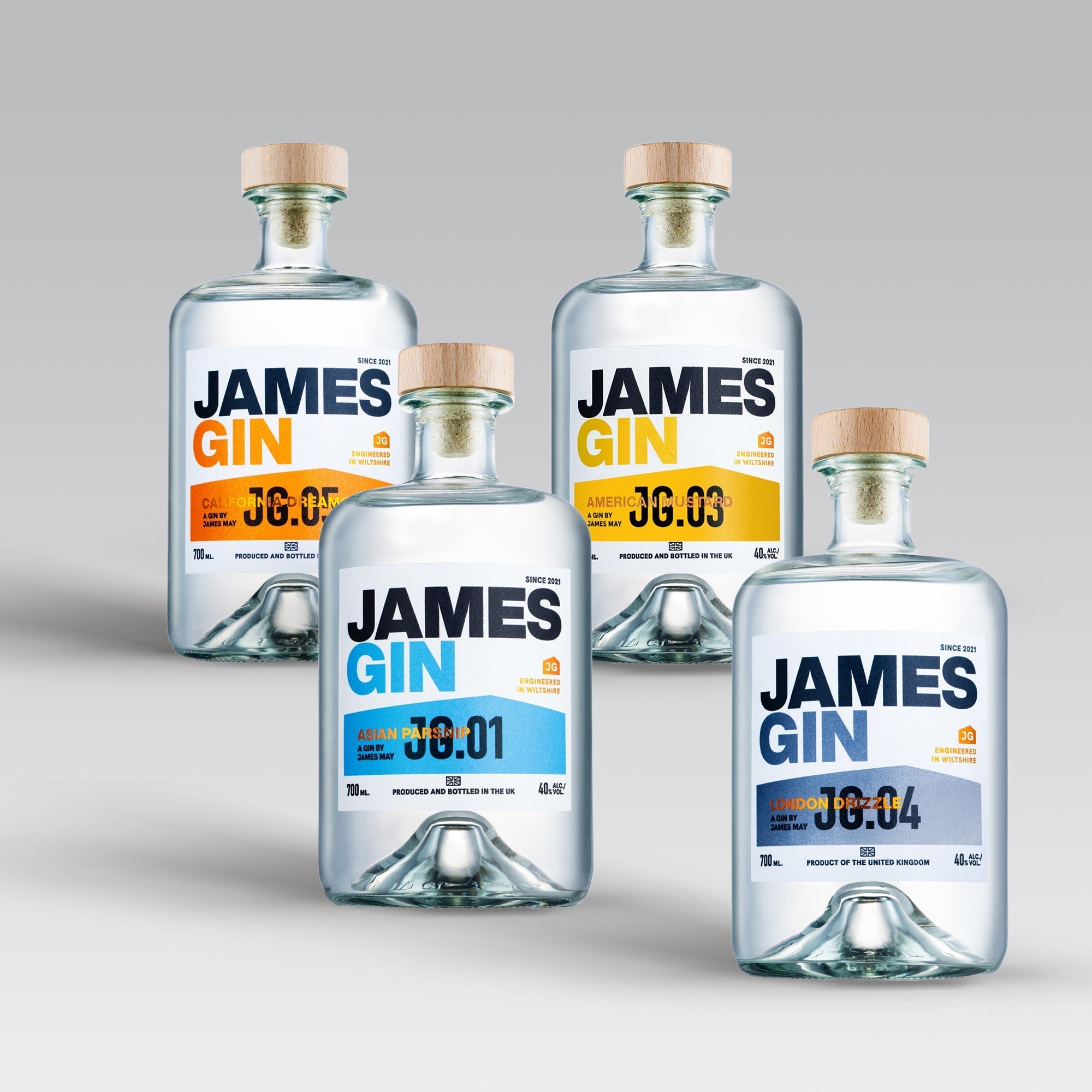 The James Gin US The Completist 4 Bottle Bundle includes four uniquely labeled glass bottles with wooden caps and a souvenir key chain, showcasing award-winning gin varieties in blue, yellow, or orange against a light gradient background.