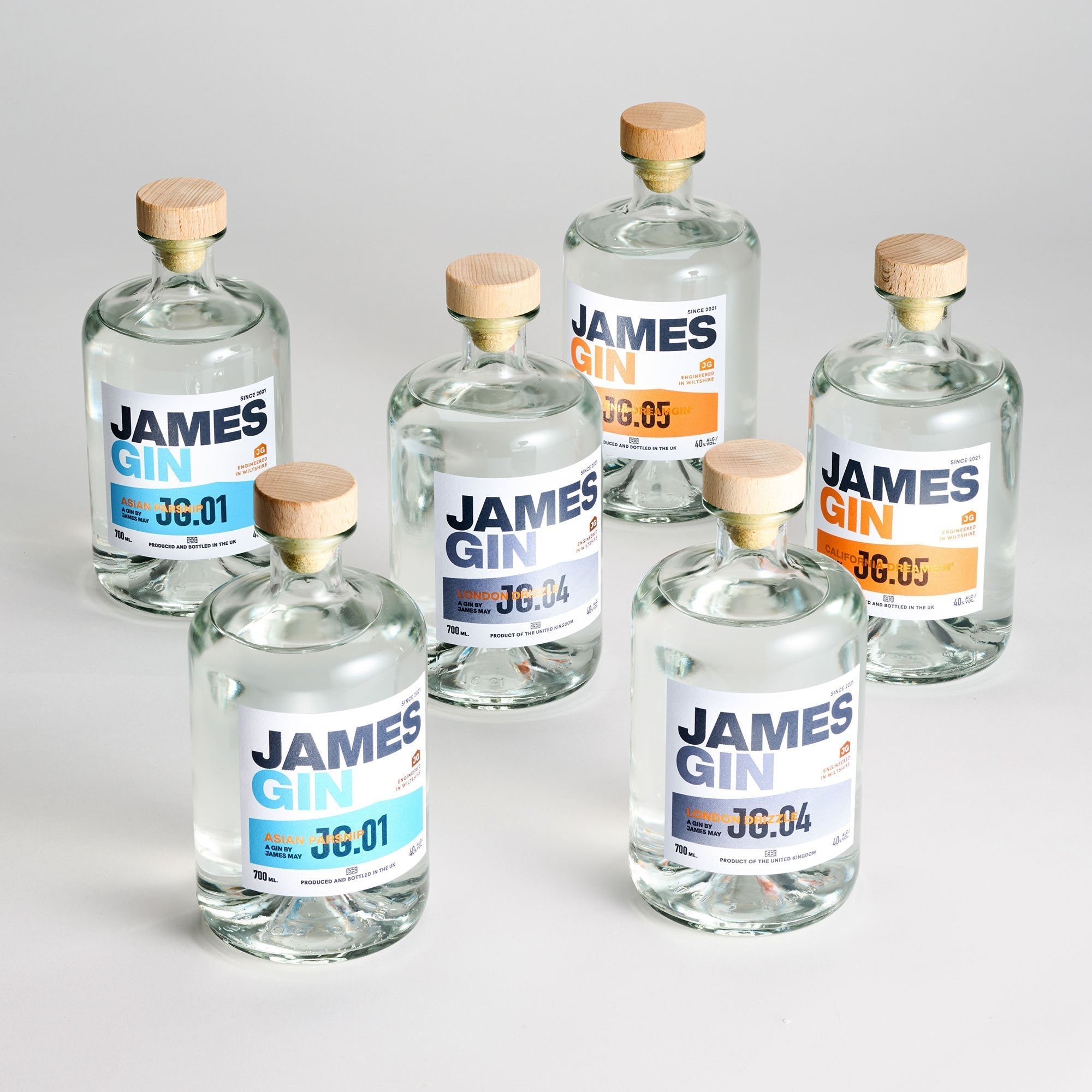 Discover the James Gin The Survivalist 6 Pack w/ Souvenir Gift Key Chain from James Gin US—six British craft gins with clear liquid, wooden caps, minimalist white labels with blue or orange accents, and unique batch numbers.