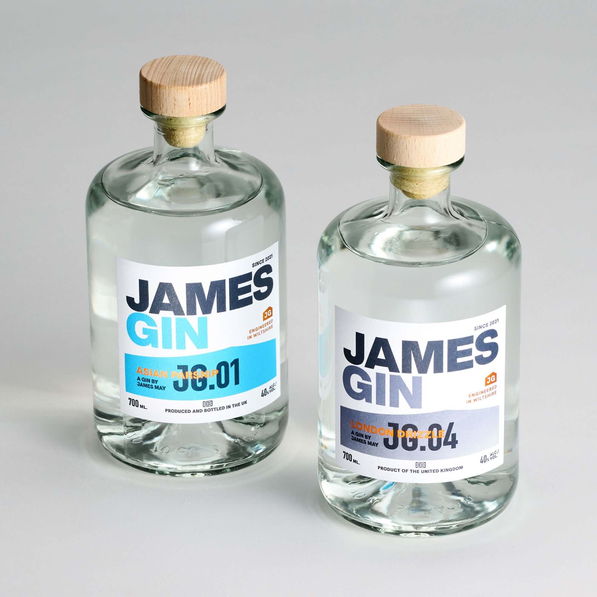 The James Gin US Starter Pack includes two clear glass bottles—Asian Parsnip 00:01 and London Dry 00:04—with wooden caps, white labels with blue and orange text, plus a souvenir gift key chain.
