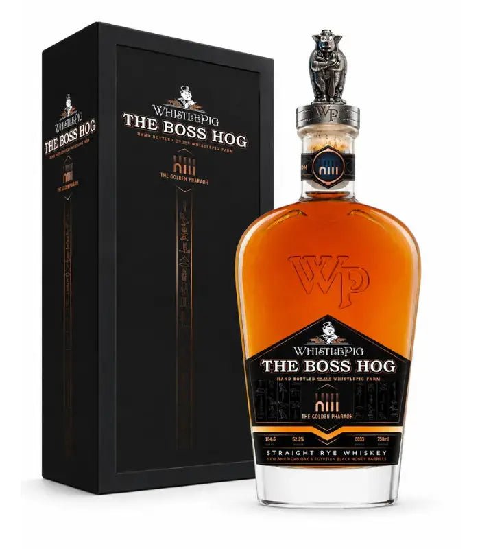 A bottle of WhistlePig The Boss Hog XIII The Golden Pharaoh Straight Rye Whiskey, adorned with a distinctive pig-shaped stopper, is displayed beside its elegant black and gold gift box, showcasing its rare finish in Egyptian Black Honey barrels.