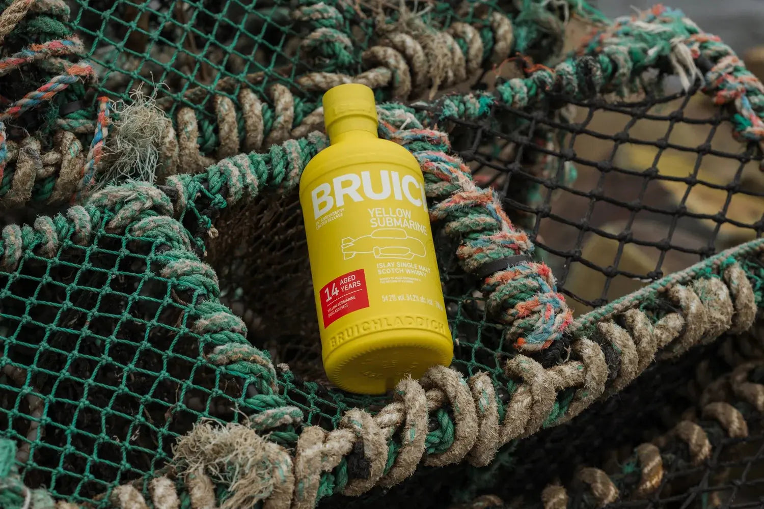 A bottle of Bruichladdich Yellow Submarine III 14 Year Old Islay Single Malt Scotch Whisky rests outdoors on stacked fishing nets with rope and mesh.