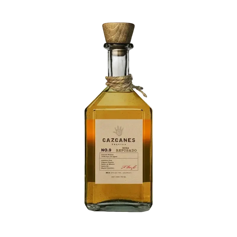 A glass bottle of Cazcanes Rosa Reposado No. 9 Tequila with a wooden stopper and a tan label detailing production information and a hand-print logo.
