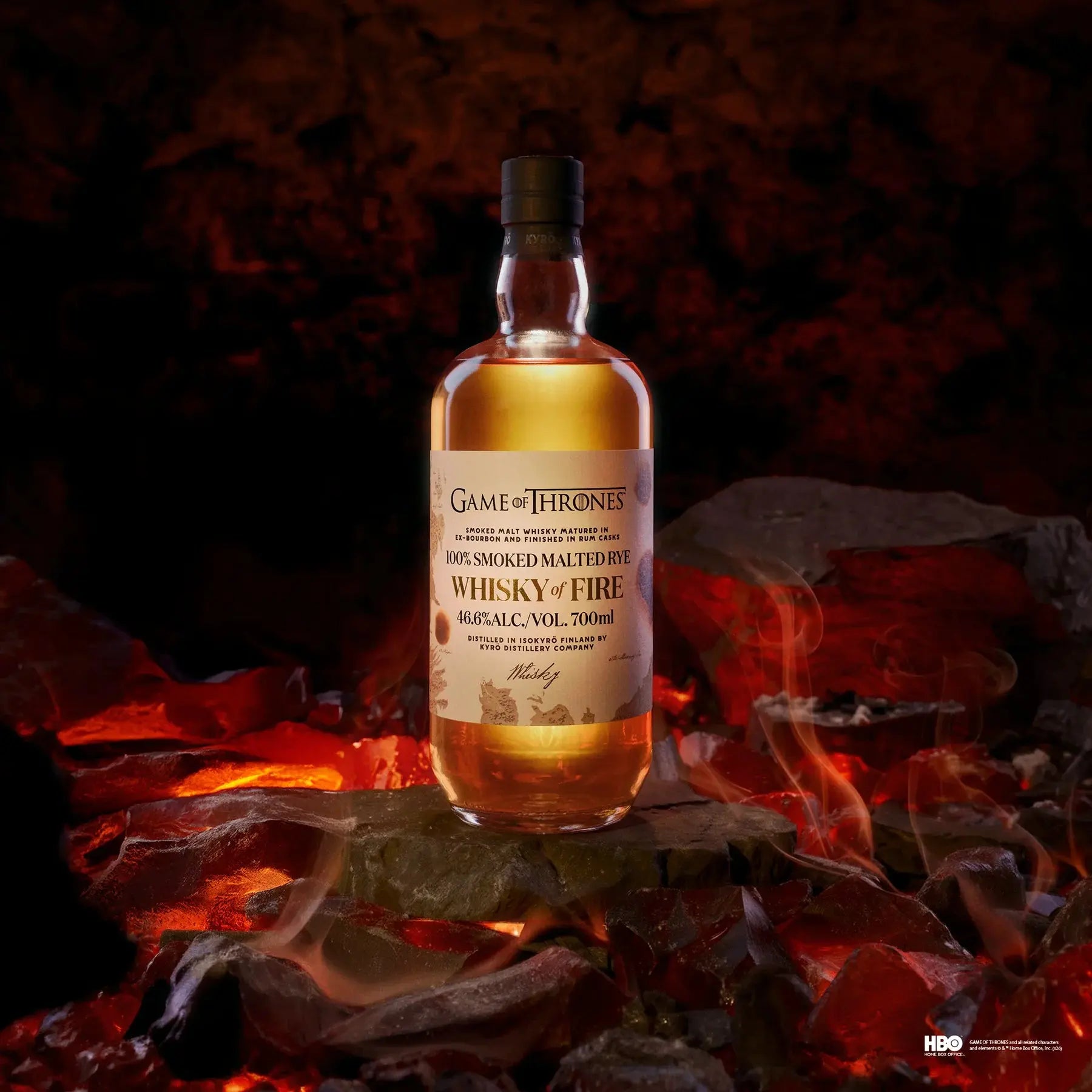 A bottle of Kyrö x Game of Thrones Whisky of Fire & Blood Bundle from Main Street Liquor stands on glowing coals amid swirling smoke, with a fiery backdrop—an epic tribute to Finnish rye whisky craftsmanship. Pre-order now!.