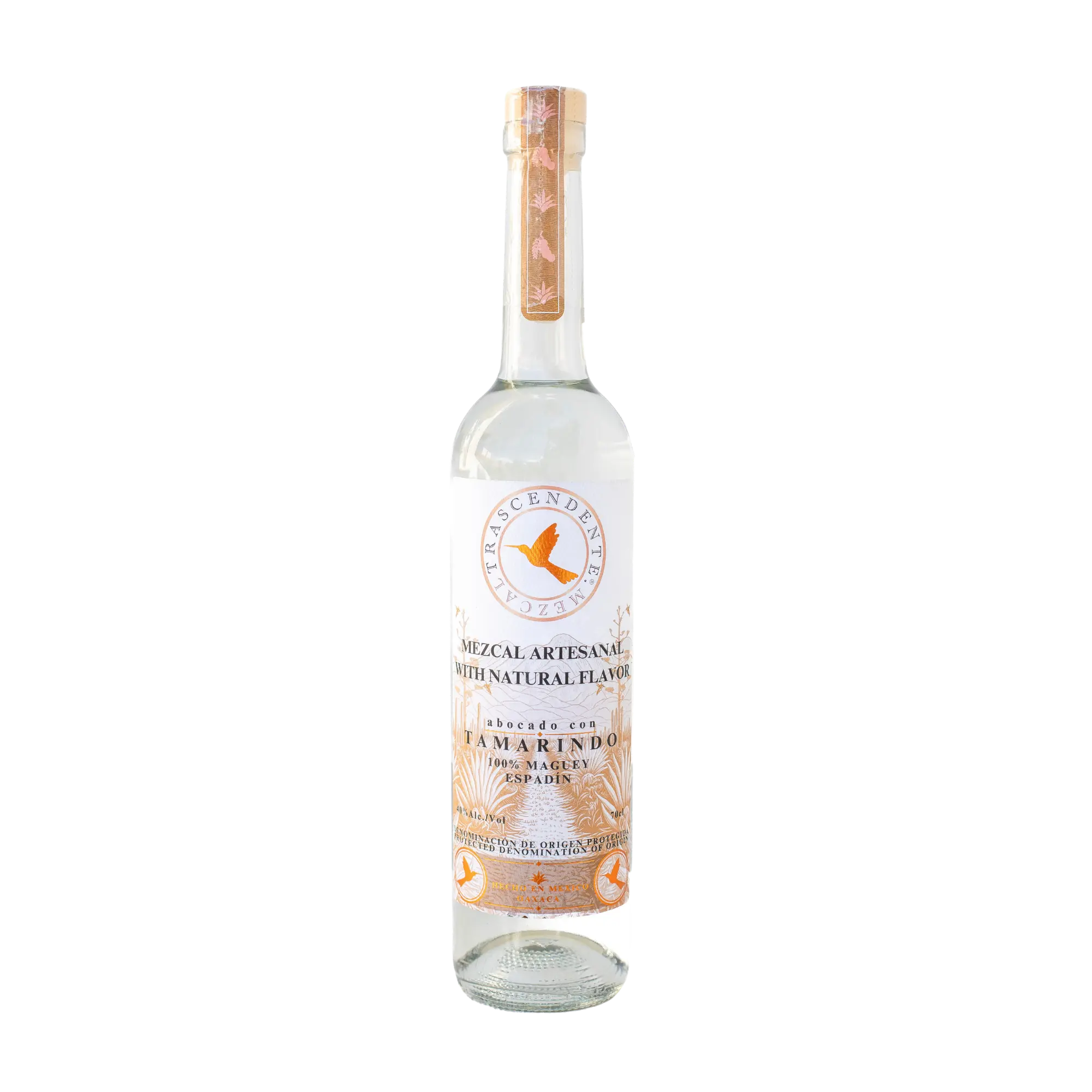 A clear glass bottle of Mezcal Trascendente Tamarindo 700ml by Mezcal Trascendente, with a white label, gold accents, wooden cap, decorative base design, and natural tamarind flavors made from Espadín mezcal.