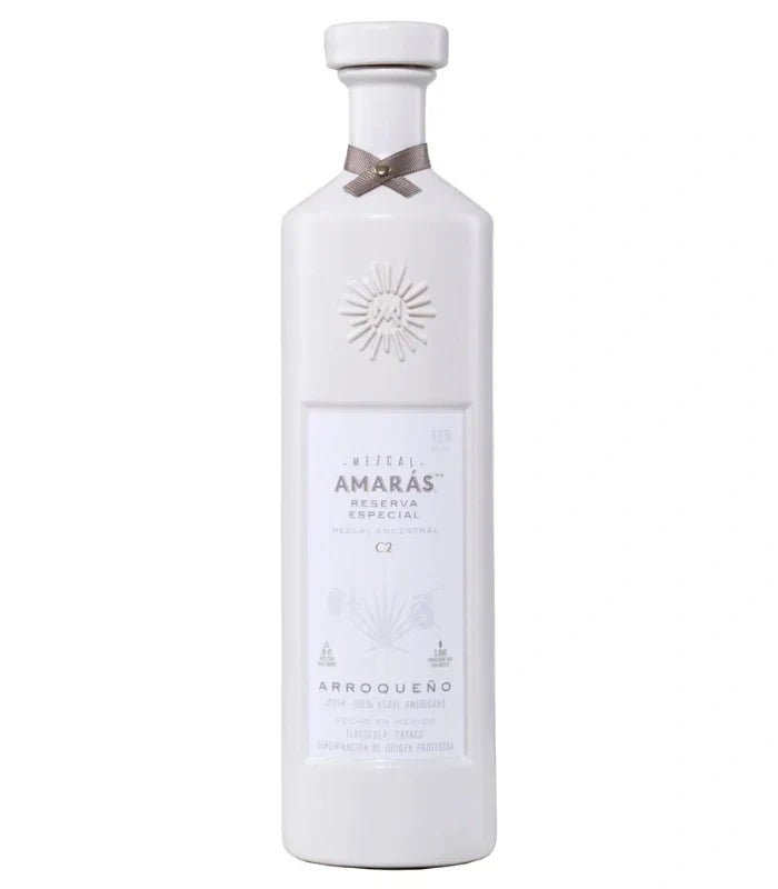 A tall, white ceramic bottle of Amaras Mezcal Joven Reserva Especial Arroqueño C2 700mL has an embossed sunburst near the neck, a silver ribbon at the top, and a minimalist label with the Amaras brand.