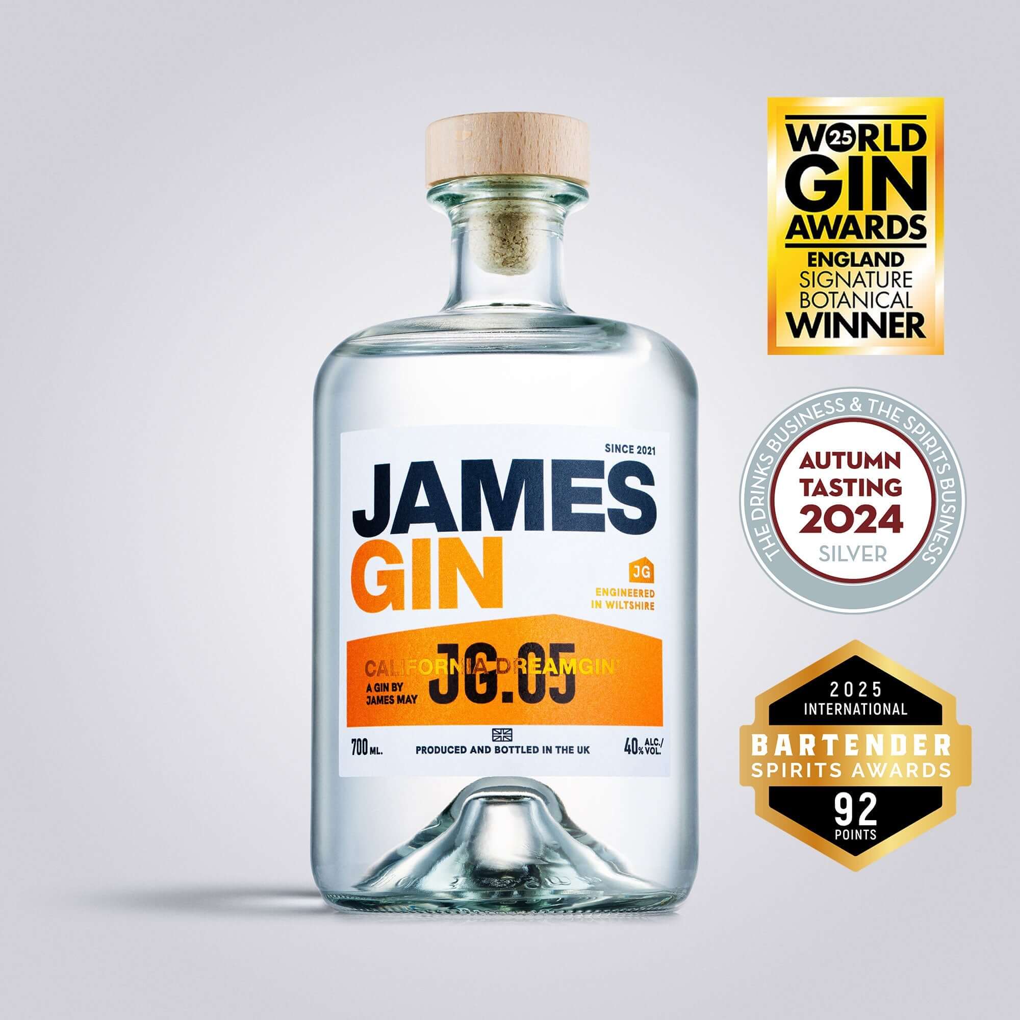 A clear glass bottle of James Gin California Dreamgin' with a wooden cap is centered, featuring orange and black text. Three award badges appear to the right, highlighting its gin competition accolades. Includes souvenir gift key chain.