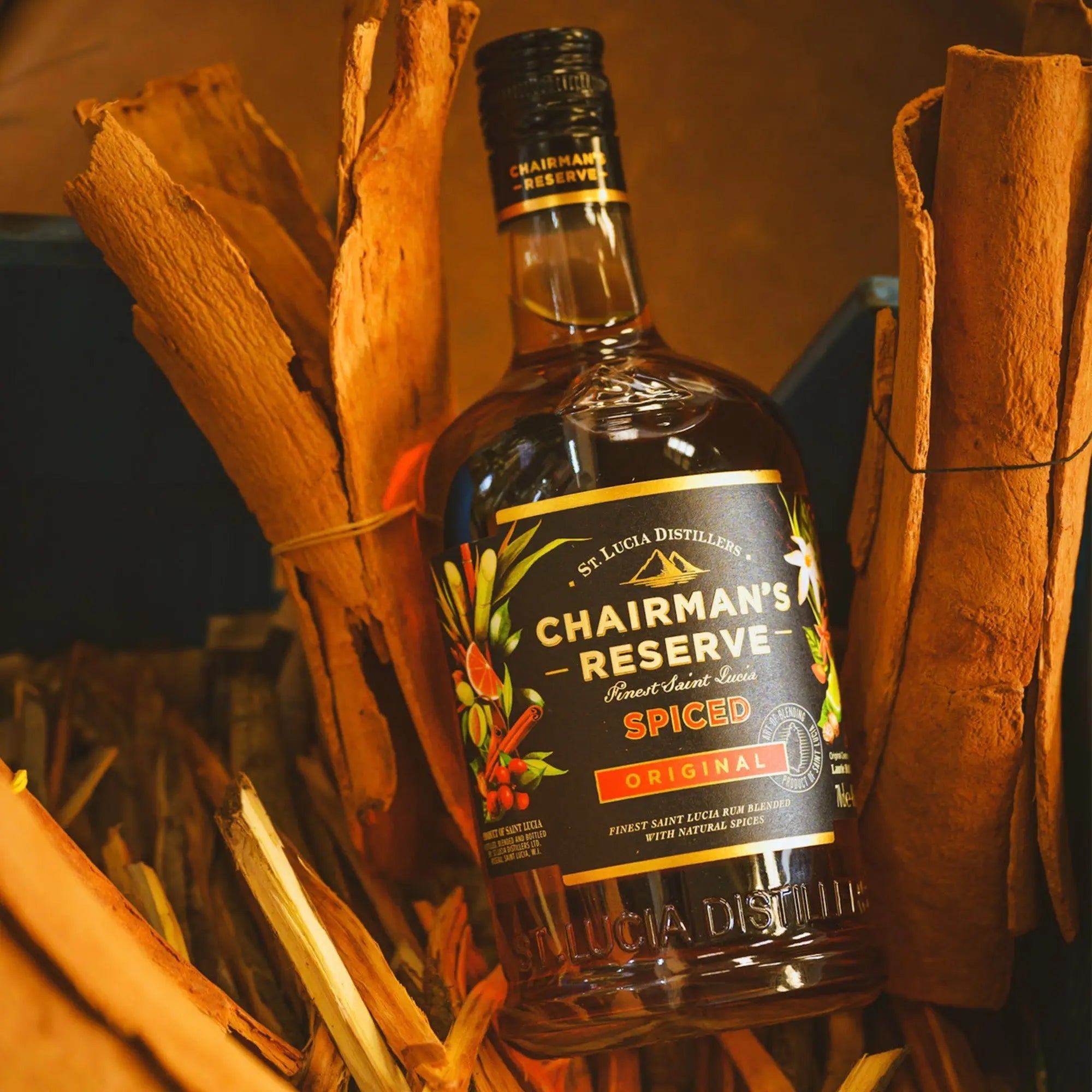 A bottle of Chairman's Reserve Spiced Original by Chairman's Reserve Rum stands upright among bundles of cinnamon sticks, its vibrant label featuring spice motifs that hint at its Caribbean origin and signature Bois Bandé infusion.