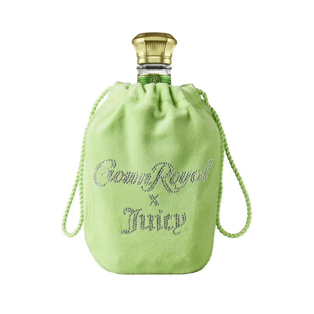 A bottle of Crown Royal Regal Apple x Juicy Couture Limited Edition, featuring a gold cap, sits inside a light green drawstring pouch adorned with sparkling "Crown Royal x Juicy" lettering—an elegant nod to this exclusive collaboration. The plain white background perfectly highlights the appeal of this apple flavored whisky from Crown Royal.