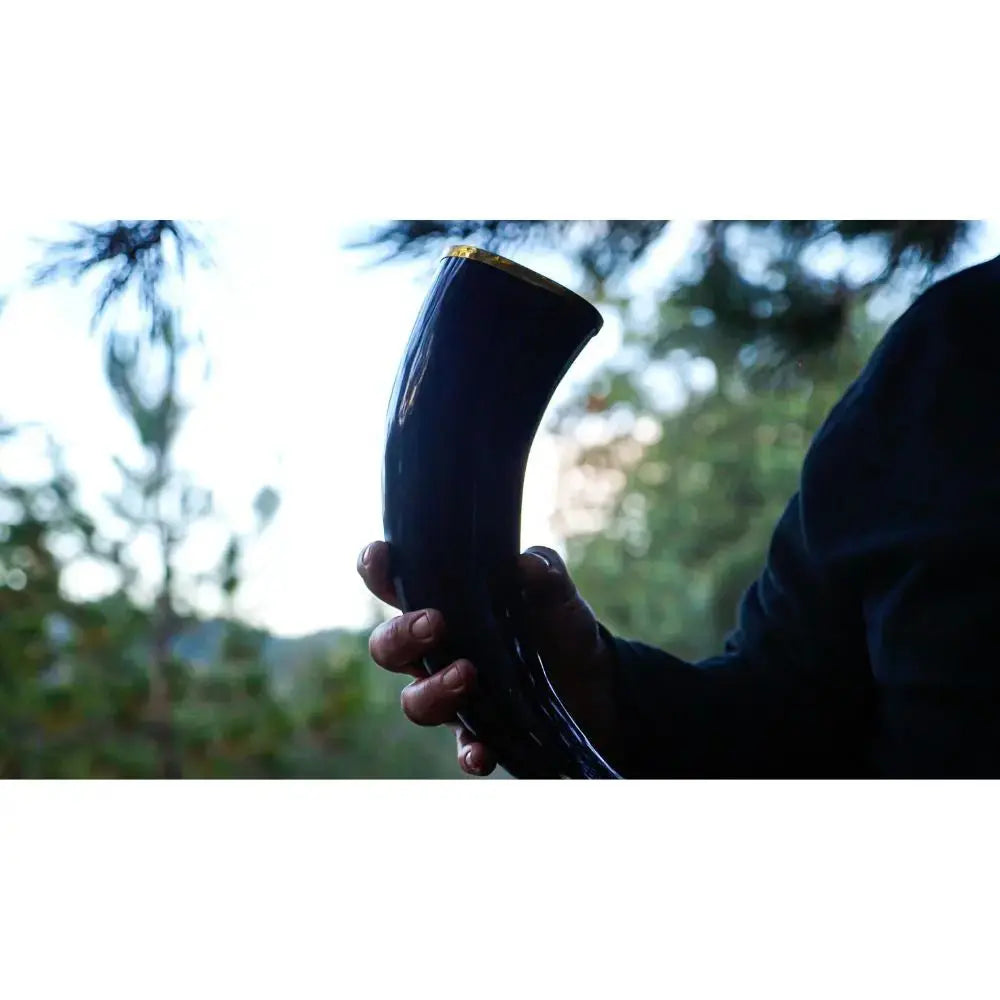 A person holds a polished black drinking horn outdoors, surrounded by blurred trees and greenery—the ideal way to savor Eldenwood Straight Bourbon Whiskey with Drinking Horn from Eldenwood.