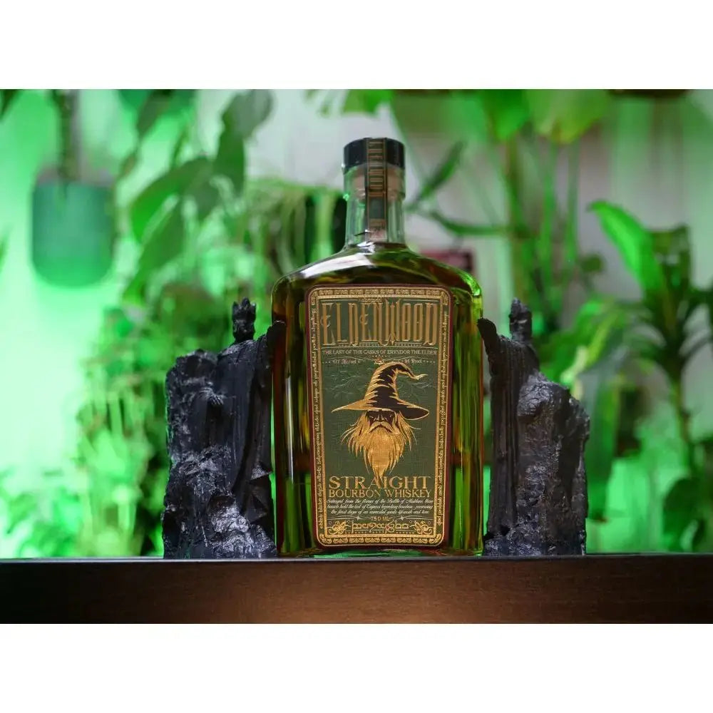 A bottle of Eldenwood Straight Bourbon Whiskey with Drinking Horn by Eldenwood sits between two dark sculpted bookends, with green plants and lighting in the background—the perfect centerpiece for any bourbon gift set.