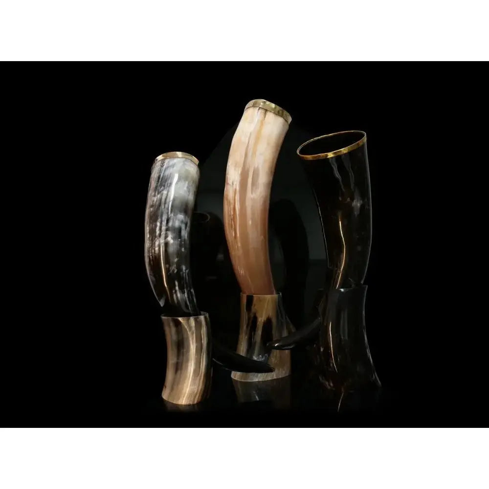 Three polished drinking horns in brown, tan, and black stand upright on holders against a black background, showcasing the Eldenwood Straight Bourbon Whiskey with Drinking Horn—an impressive bourbon gift set from Eldenwood, ideal for savoring fine whiskey.