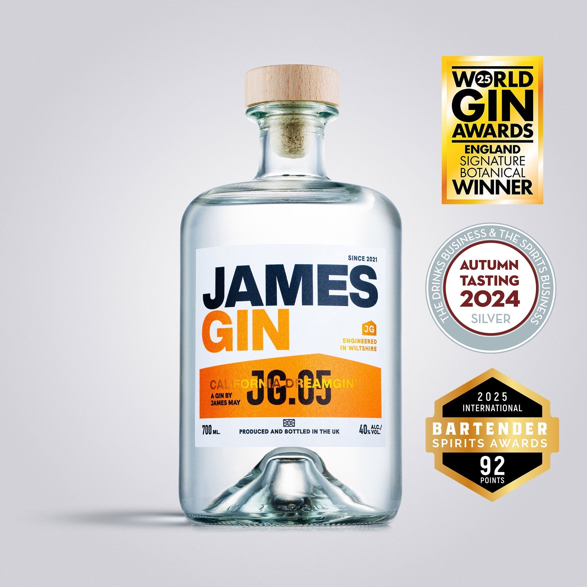 A clear glass bottle of James Gin California Dreamgin' with a wooden cap is centered, featuring orange and black text. Three award badges appear to the right, highlighting its gin competition accolades. Includes souvenir gift key chain.