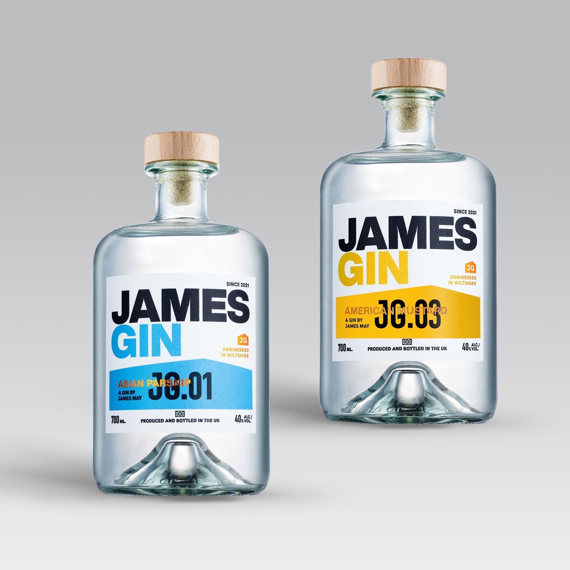Two clear James Gin US bottles from the James Gin The Hedge 2 Bottle Bundle with wooden caps and labels—one blue-accented “Asian Parsnip 00:01,” one yellow “American Mustard 00:03”—are displayed with a souvenir gift key chain.