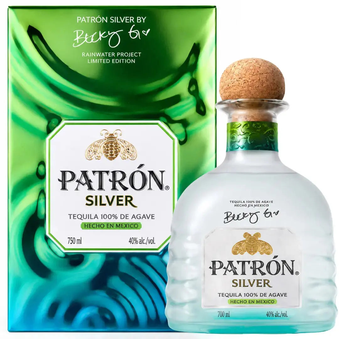 A bottle of Patron Silver Isla Urbana x Becky G Frosted Bottle Limited Edition Tequila 700mL, from Patron and crafted from 100% Weber Blue Agave with a signature cork top, is displayed in front of its green and blue box featuring the Becky G Frosted Bottle and Rainwater Project Limited Edition text.