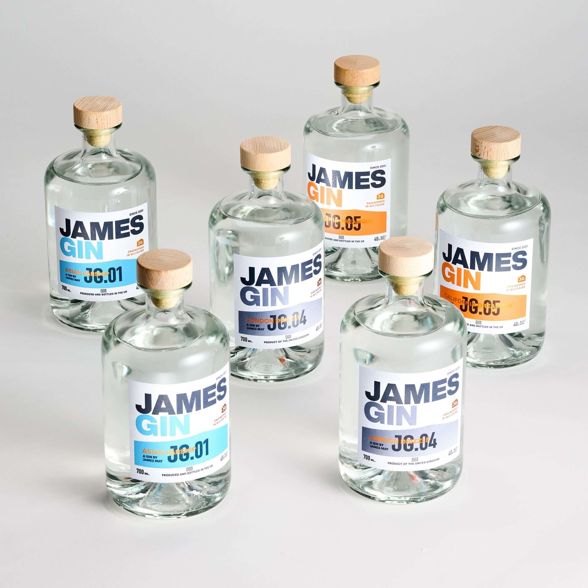 Discover the James Gin The Survivalist 6 Pack w/ Souvenir Gift Key Chain from James Gin US—six British craft gins with clear liquid, wooden caps, minimalist white labels with blue or orange accents, and unique batch numbers.