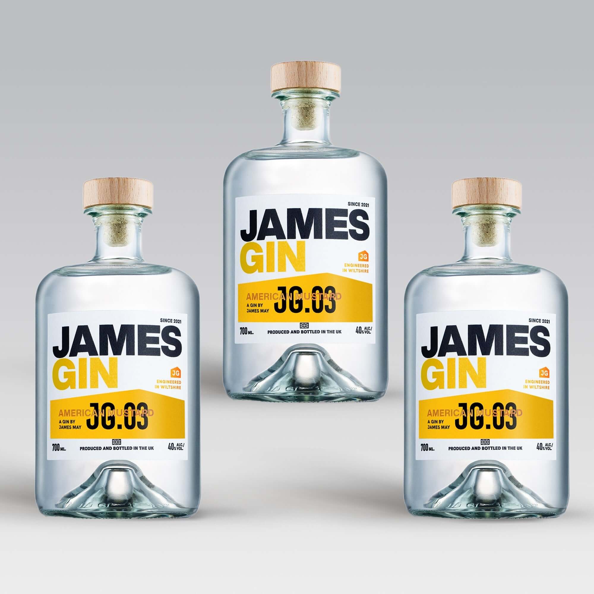 Three bottles of James Gin US "The Big, Beautiful Bundle" with wooden caps are arranged in a triangle on a light gray background. Each features a white label with bold black and yellow text, plus a souvenir gift key chain.